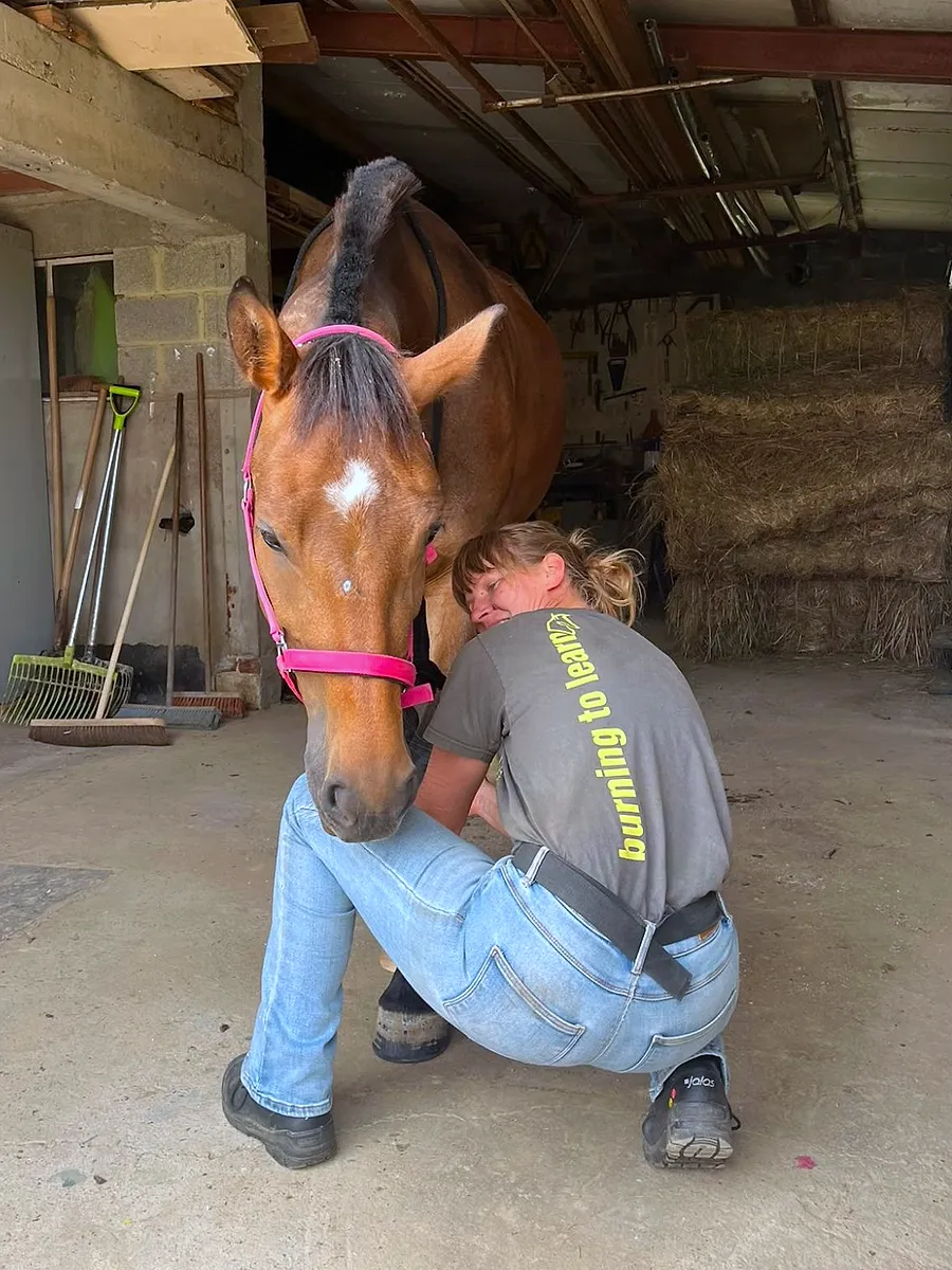 Veera zit gehurkt naast een paard dat ontspannen het hoofd laat zakken